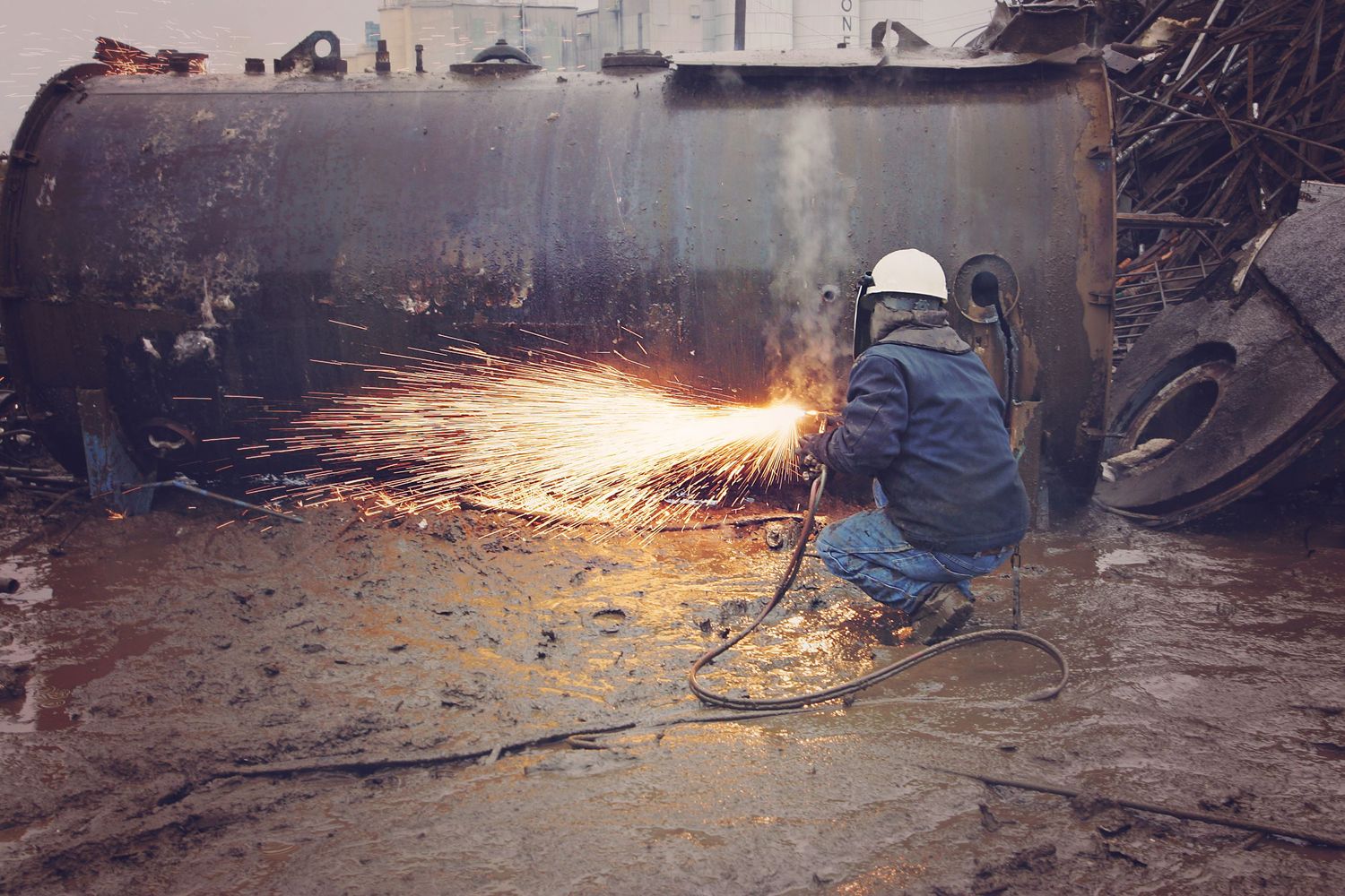 Worker using torch to cut metal in industrial setting creating bright sparks.