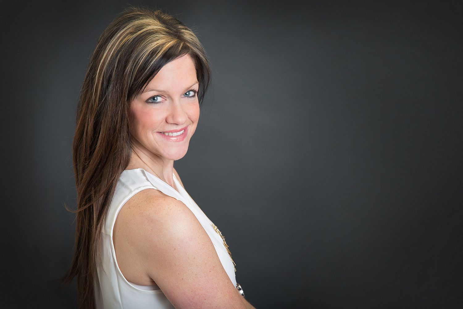 Professional portrait of woman in white sleeveless top against dark background.