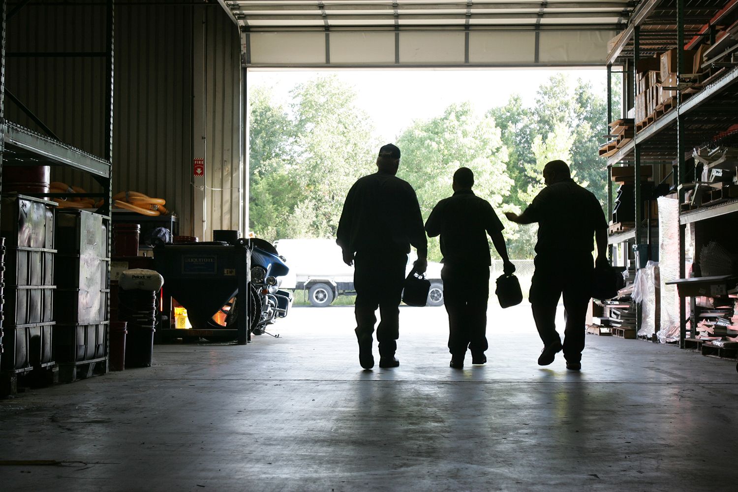 Silhouette of three workers walking through warehouse loading dock.