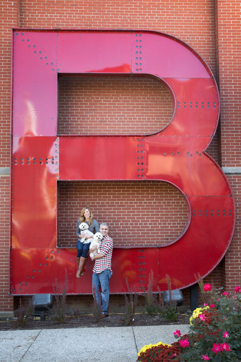Couple posing playfully against large red letters on brick wall.