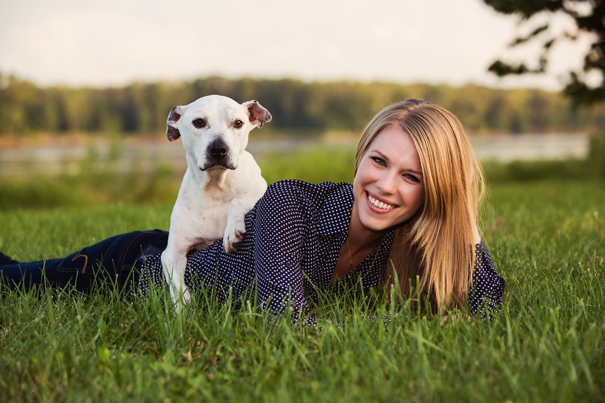 Professional lifestyle portrait in a sunlit grassy field with a dog.
