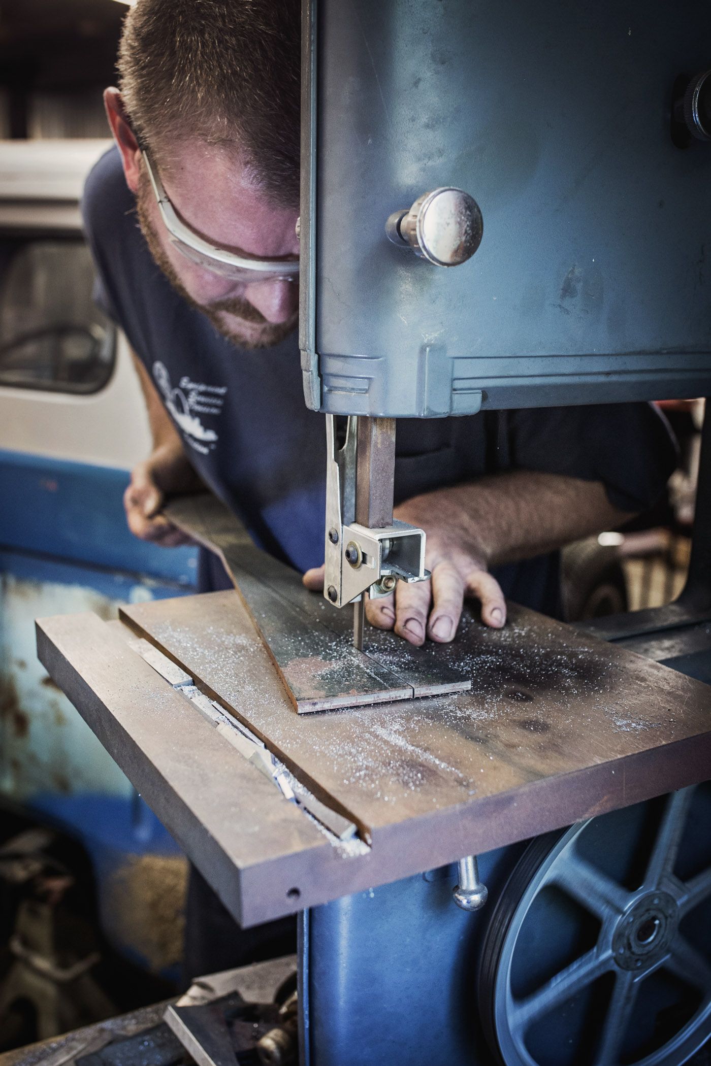 Person wearing safety glasses operates industrial bandsaw machine while working in workshop.