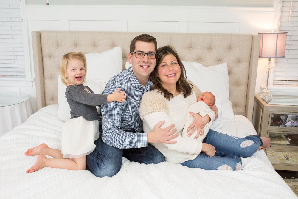 Family relaxing together on white upholstered bed.