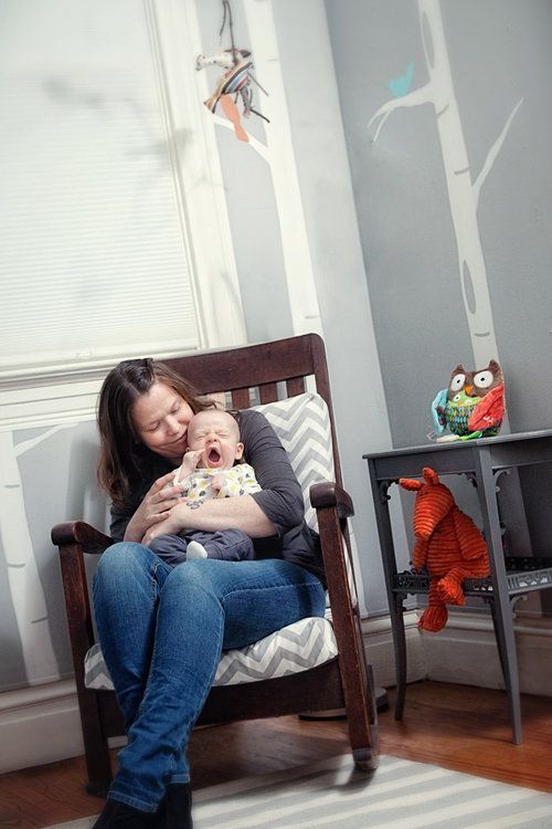 Mother and baby share a tender moment in a cozy nursery room with woodland decor.