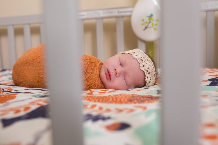Sleeping newborn with lace headband in crib with orange and white bedding.