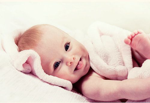 Dreamy side profile portrait of baby wrapped in soft pink blanket against white background.