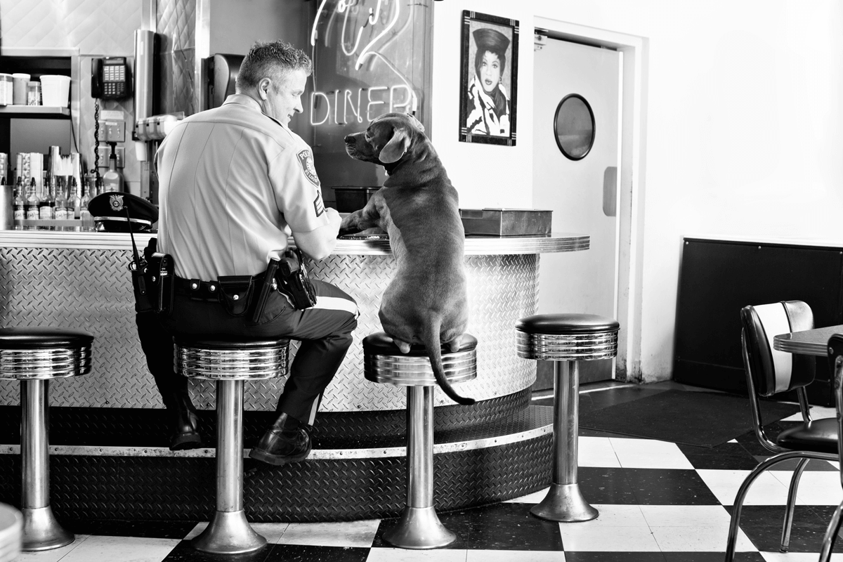 Vintage black and white photo of dog sitting next to customer at diner counter.