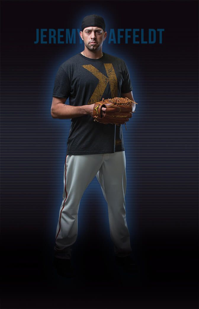 Baseball player in dark jersey and grey pants poses with glove against blue background.