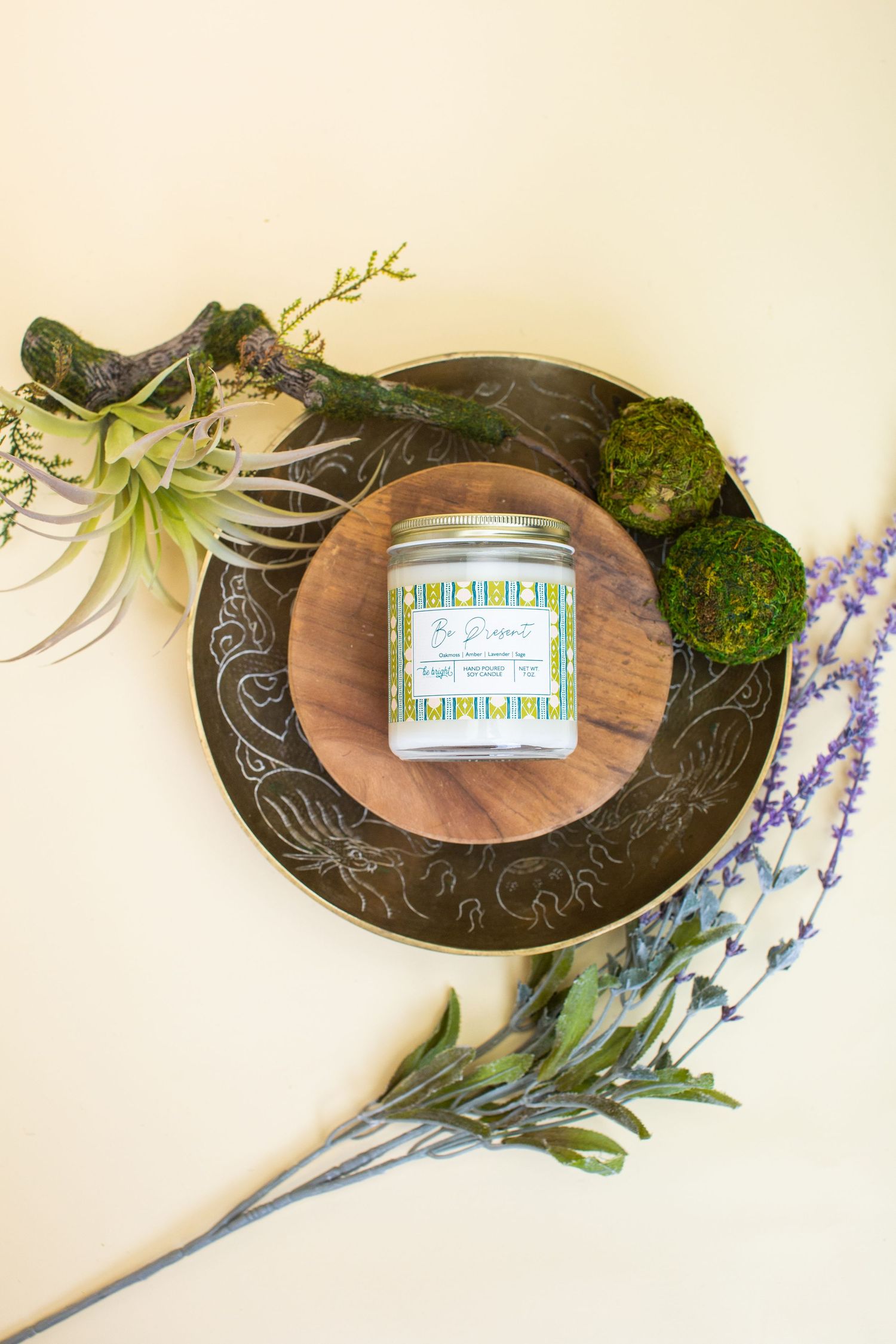Decorative candle jar surrounded by moss balls and air plants on ornate plate.