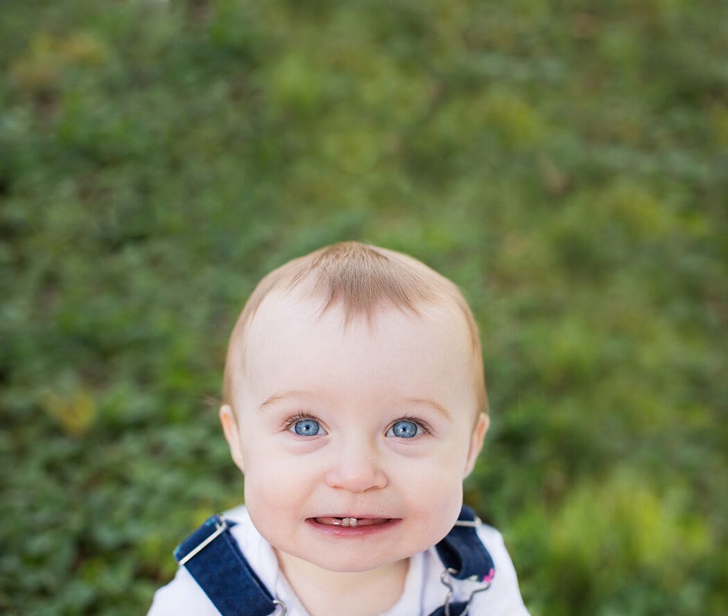 Close-up portrait with bright blue eyes and charming smile against natural green background.