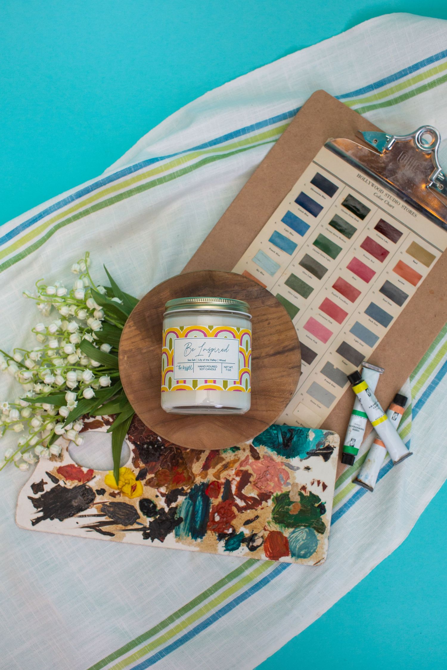Decorative candle jar displayed with floral elements and color palette on turquoise background.
