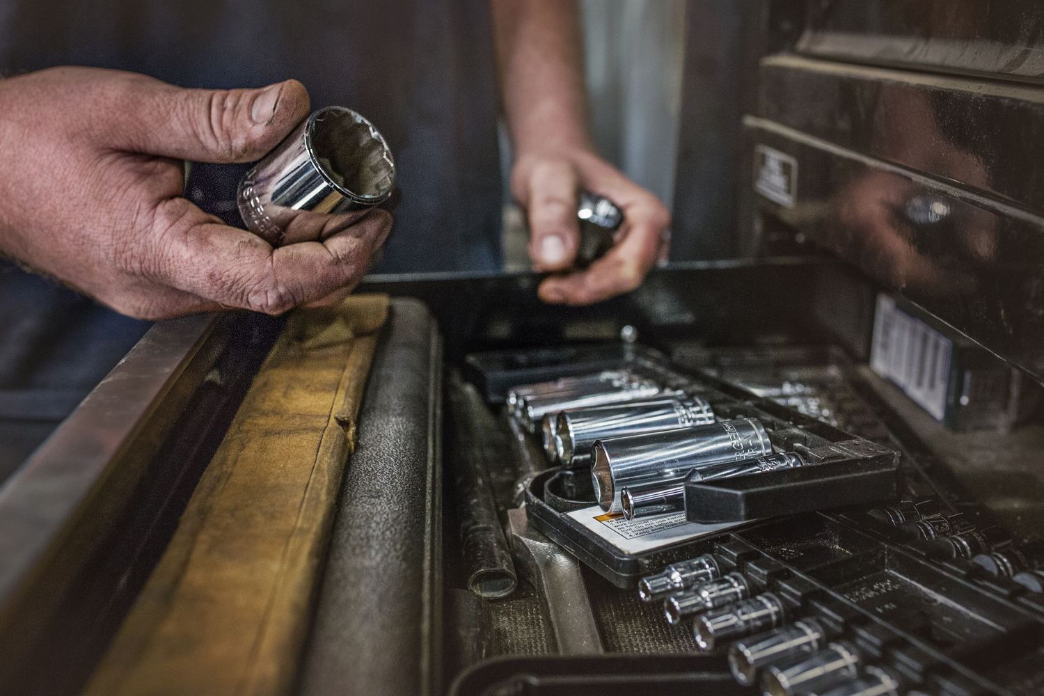 Close up of hands organizing metal tools in a workshop drawer.