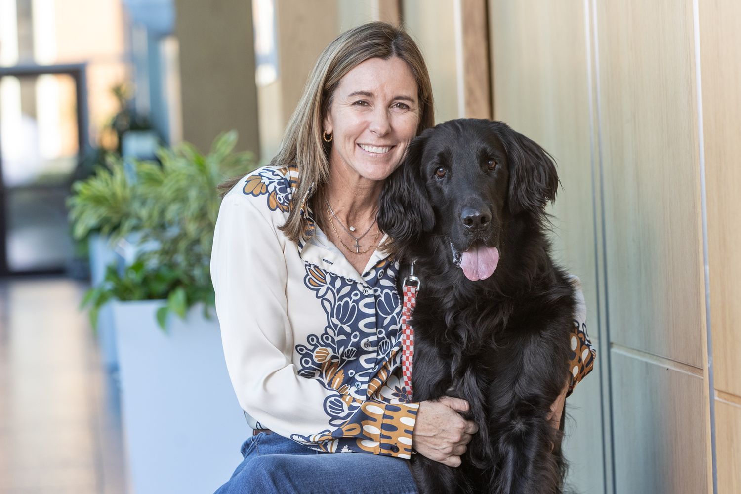 A black Labrador dog sitting beside their companion against a light colored wall.
