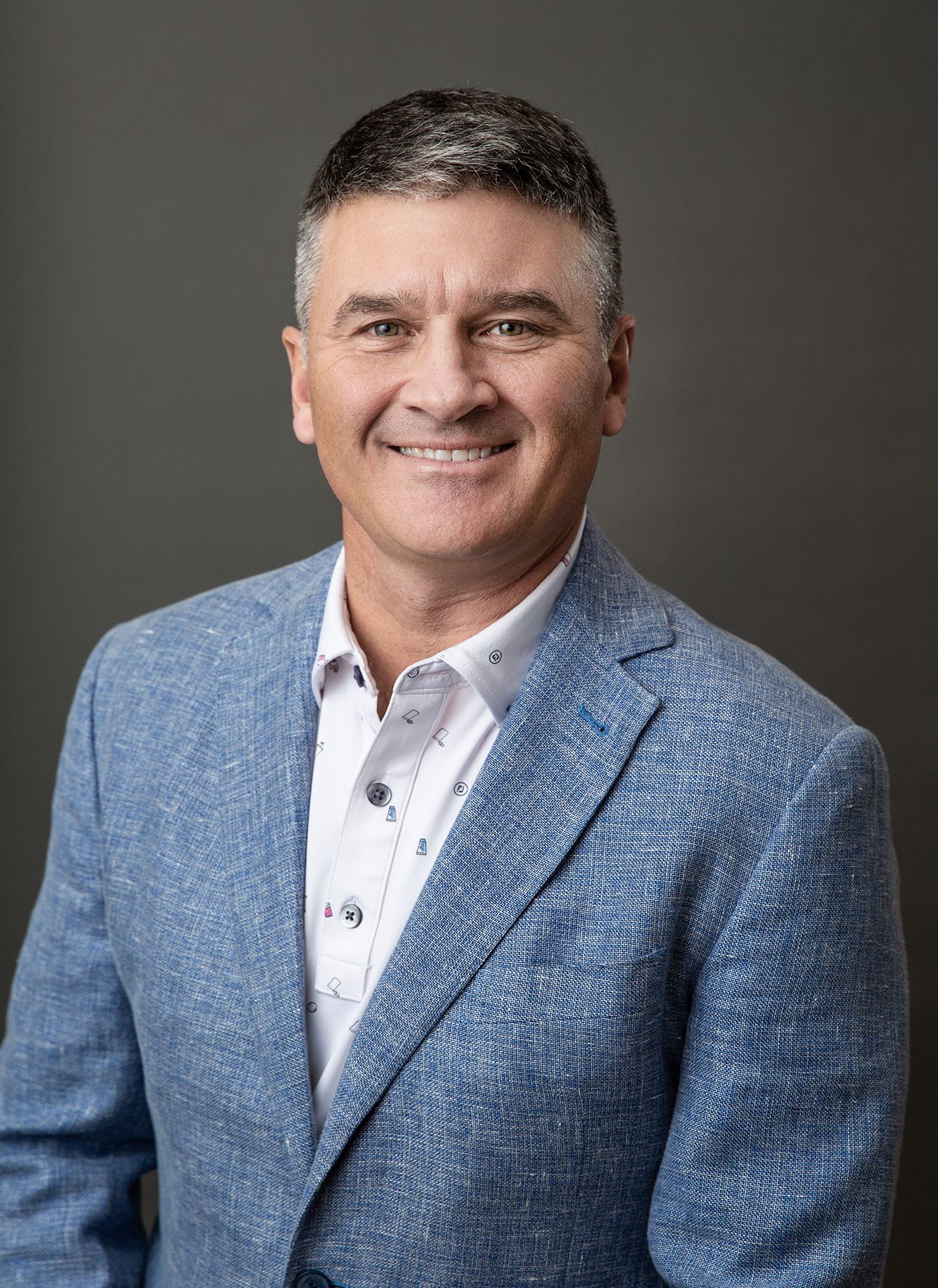 Professional headshots of person in blue blazer against dark background.