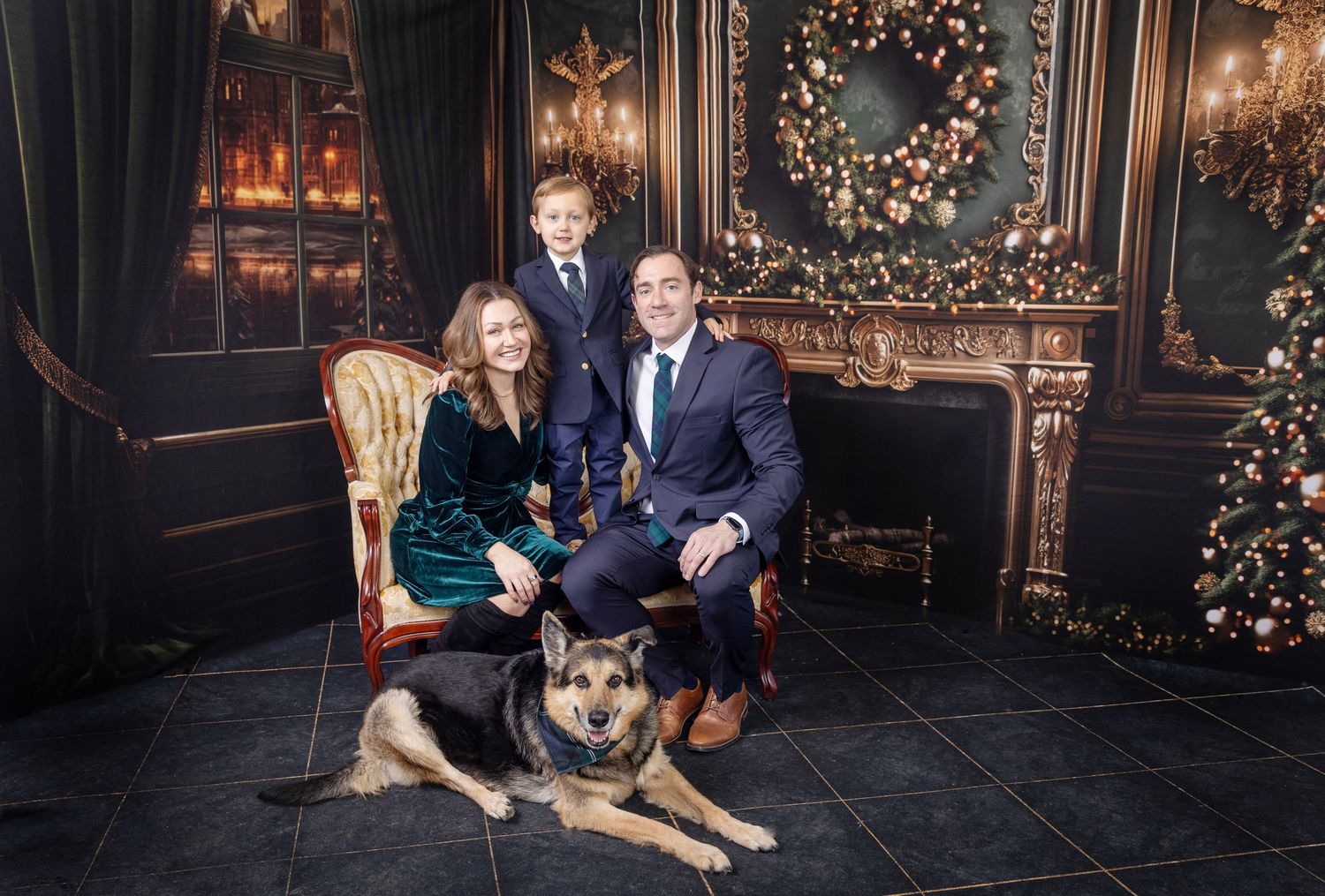 Family Christmas portrait with parents, child, and German Shepherd dog posed in elegant holiday decorated room.