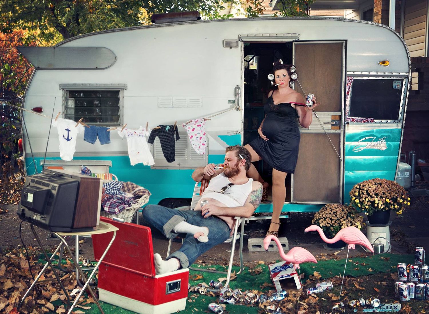 A vintage turquoise camper trailer decorated with pink flamingos and outdoor furniture.