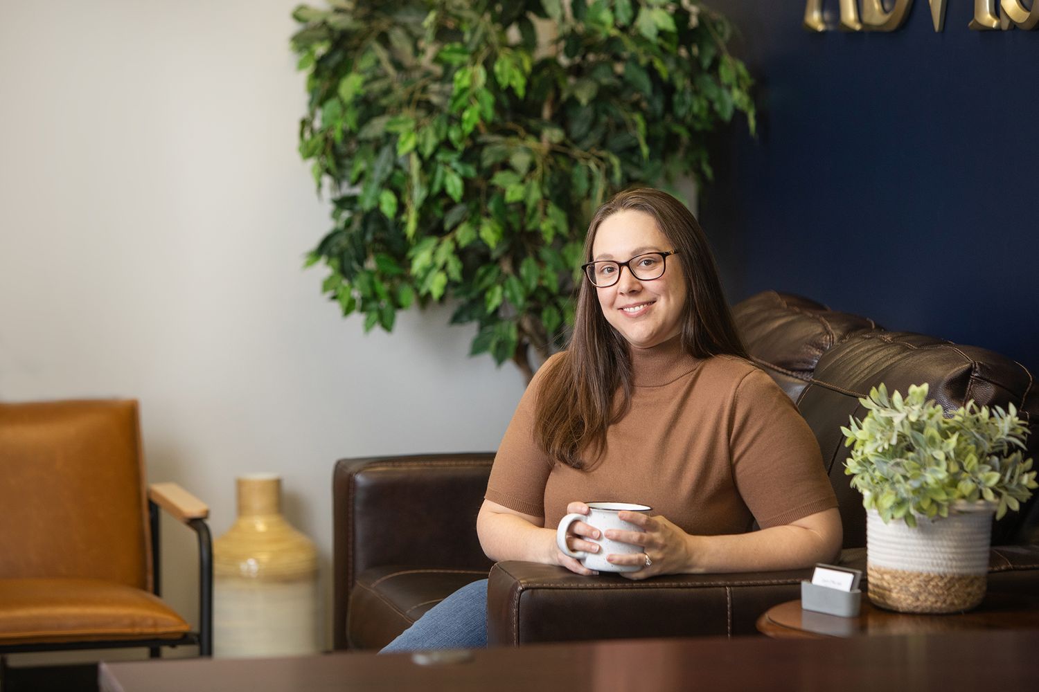 Person relaxing in modern office space with coffee cup and indoor plants.
