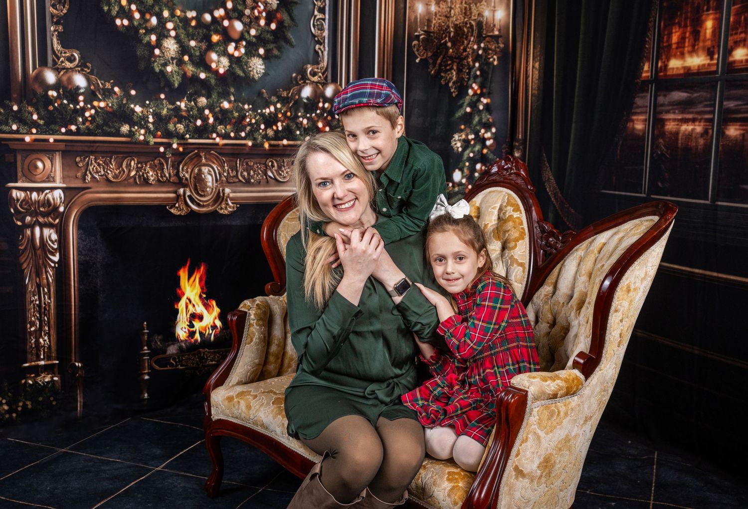 Family Christmas portrait with mother and two children by decorated fireplace and tree.