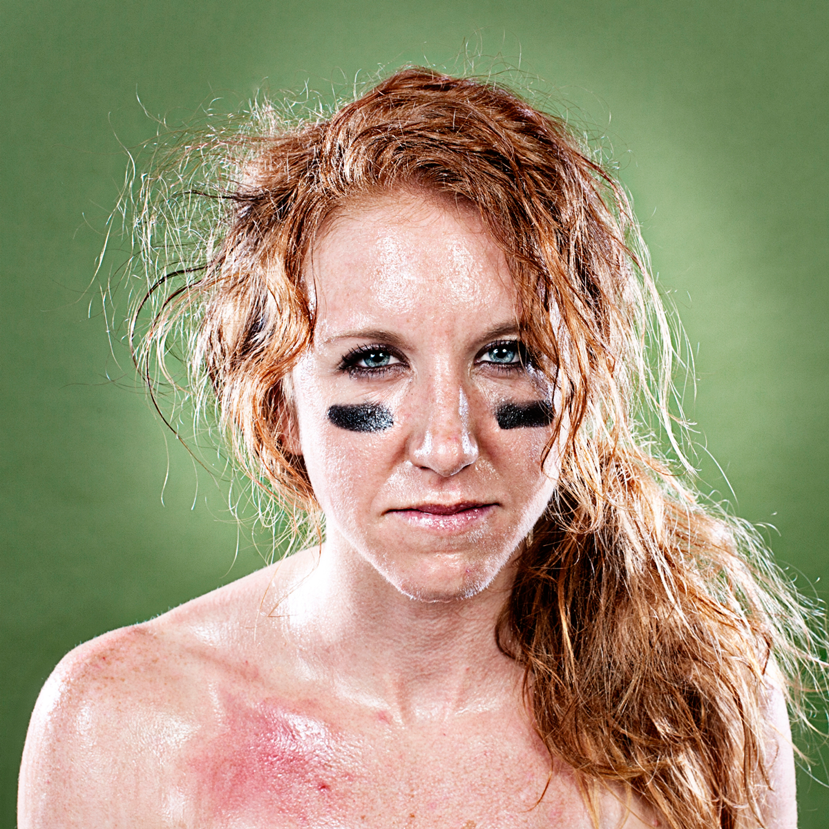 Athletic individual with eye black and wet hair against green background.
