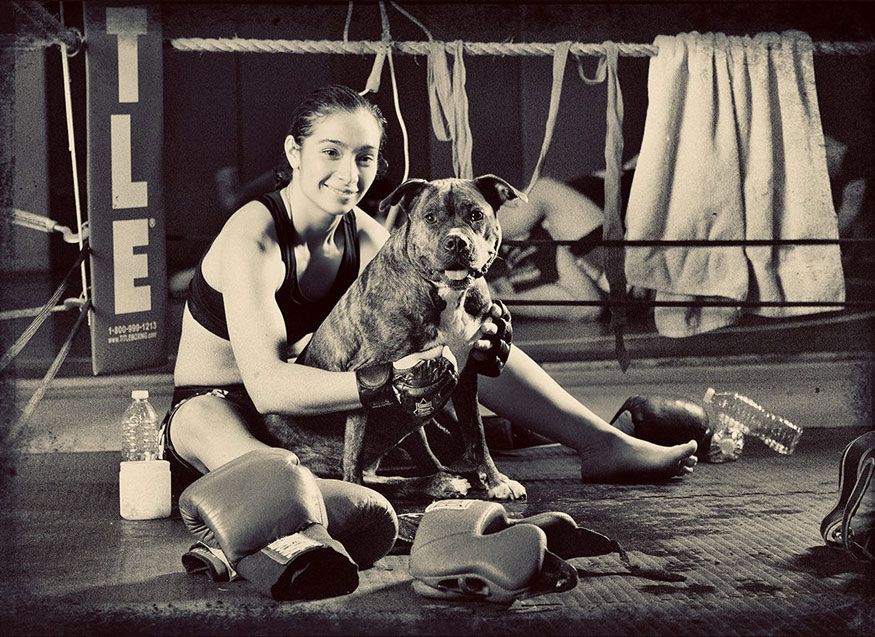 Vintage black and white photo showing someone in athletic attire playing with a boxer dog on the floor.