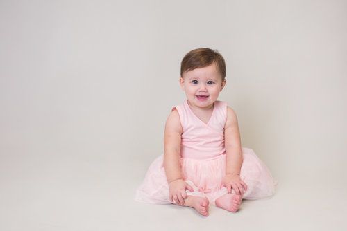 Baby in pink tutu dress sitting on white backdrop during studio photo session.