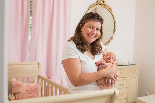 Nursery scene with gold mirror and pink curtains showing parent holding newborn.