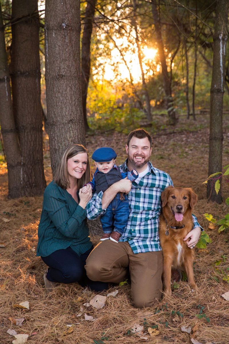 A family and their golden retriever pose together in a sunlit forest during autumn.