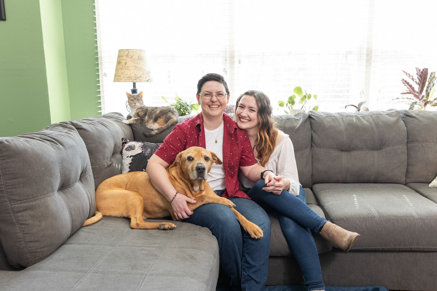 Two people sitting on a gray sectional sofa with a golden-brown dog in a cozy living room.