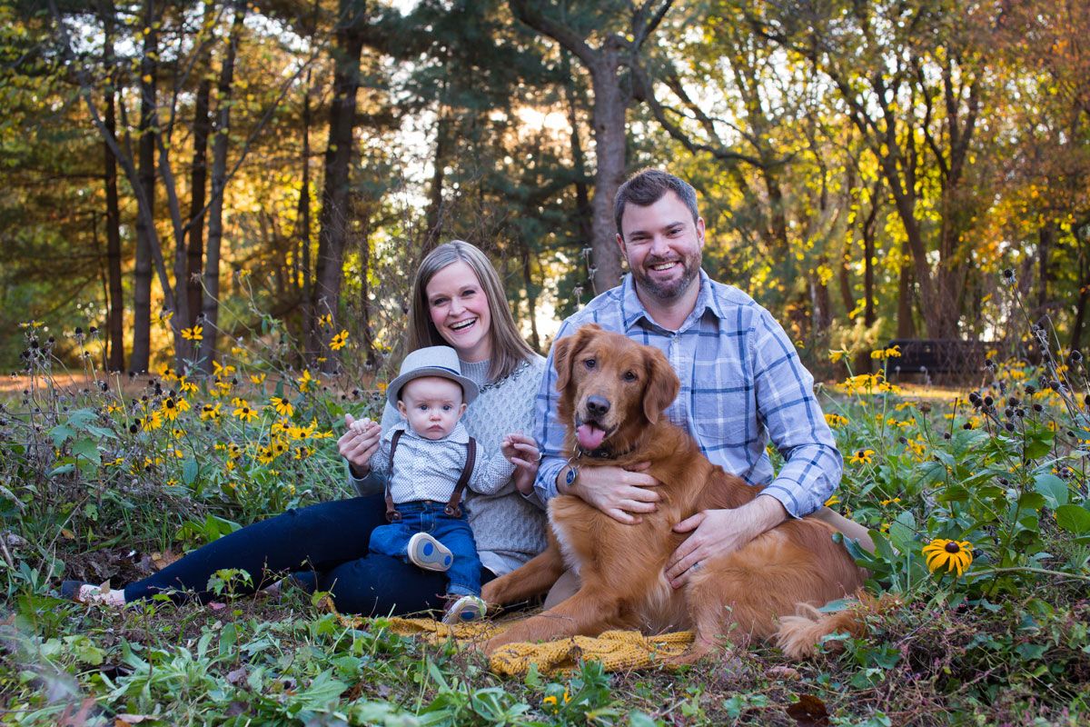 Family and golden retriever relaxing in fall foliage during outdoor photoshoot.