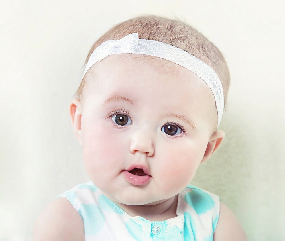 Baby wearing white headband and mint sleeveless dress looking directly at camera.