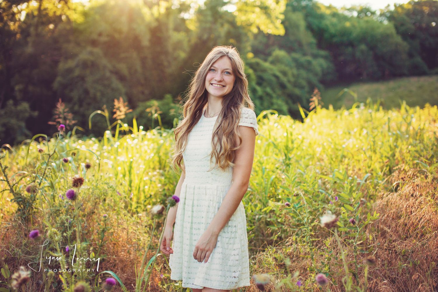 Young woman in white dress smiling in a sunlit wildflower meadow with golden hour lighting.