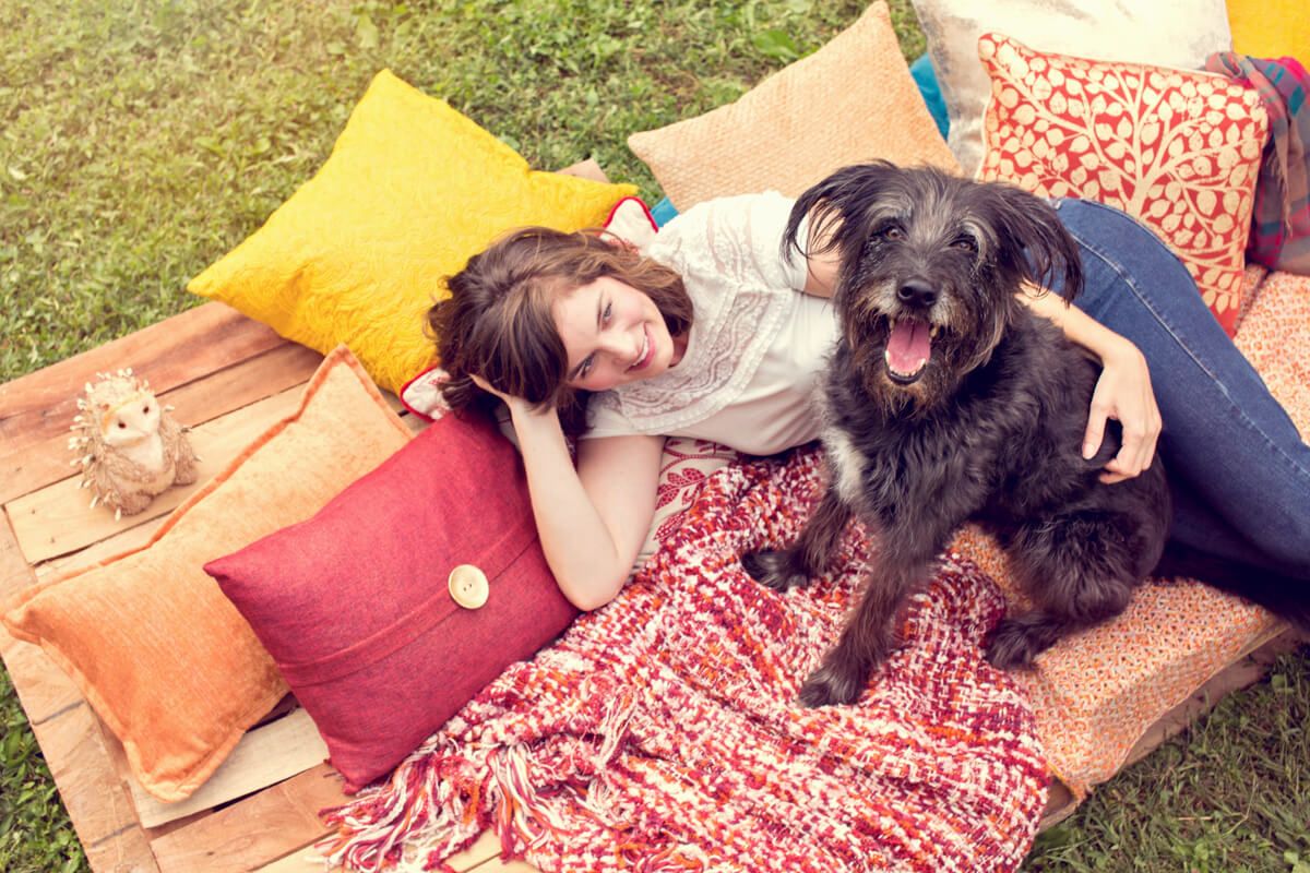 A relaxed outdoor scene with a dog and owner lounging on cushions and blankets in the grass.