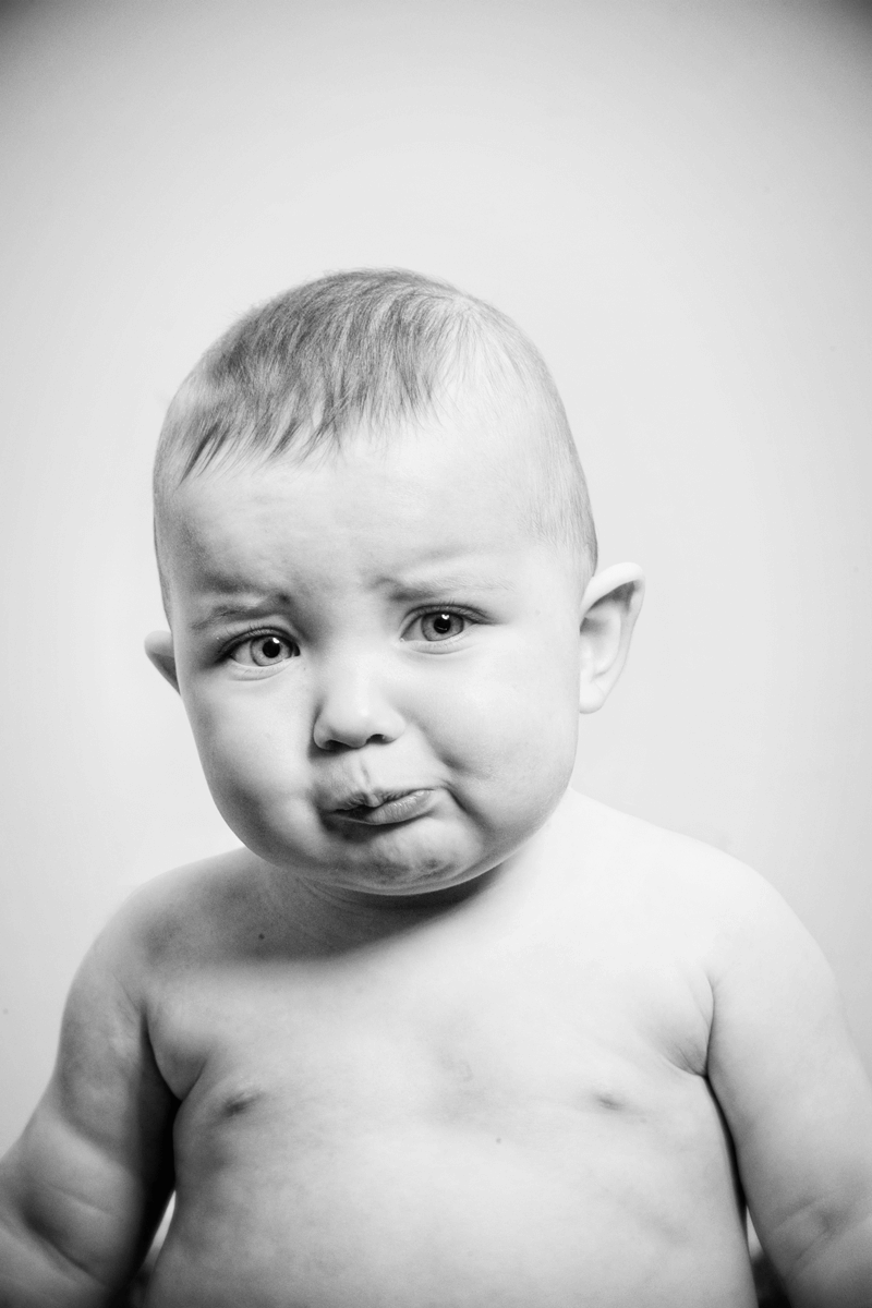 Black and white portrait of baby making pouty expression against plain background.
