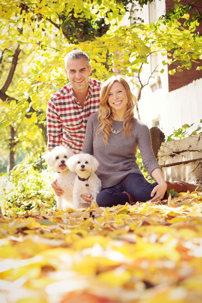 Couple with white dogs sitting among fallen autumn leaves in sunlight.