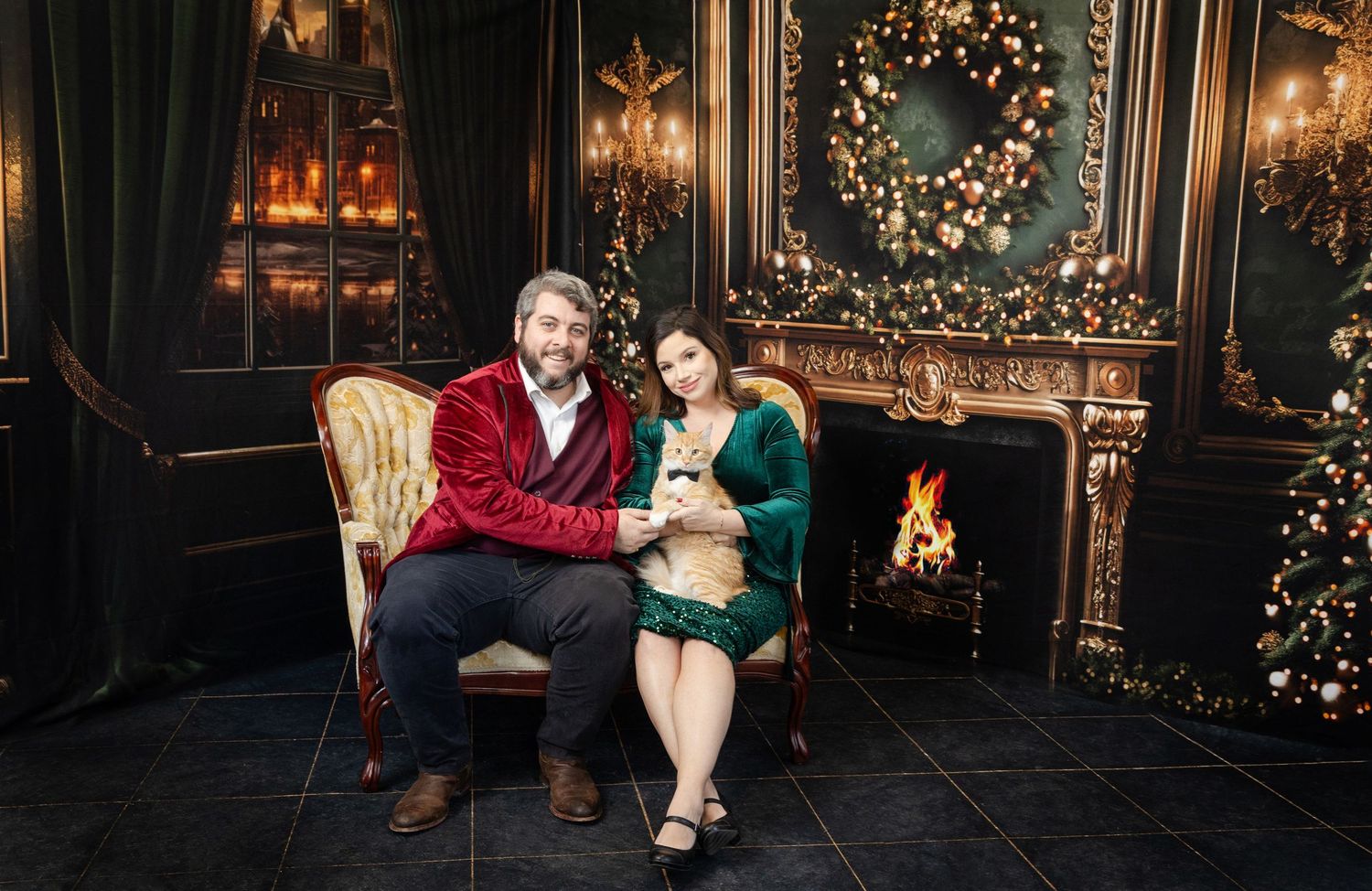Couple in festive red and green outfits sitting by a decorated fireplace with Christmas wreath and tree.