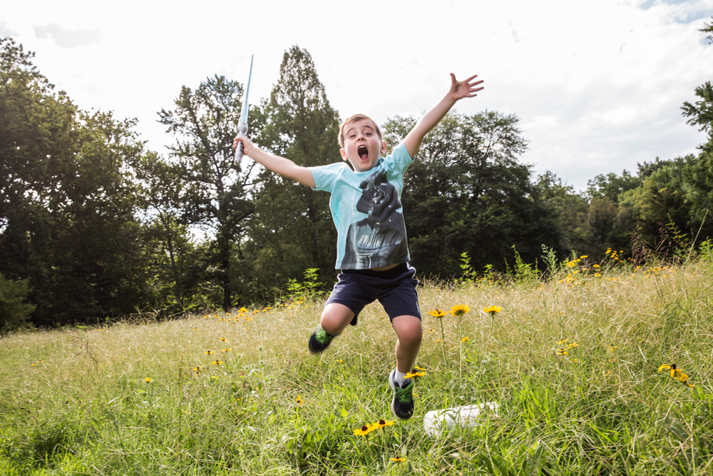 Child jumping with joy in meadow filled with yellow wildflowers.