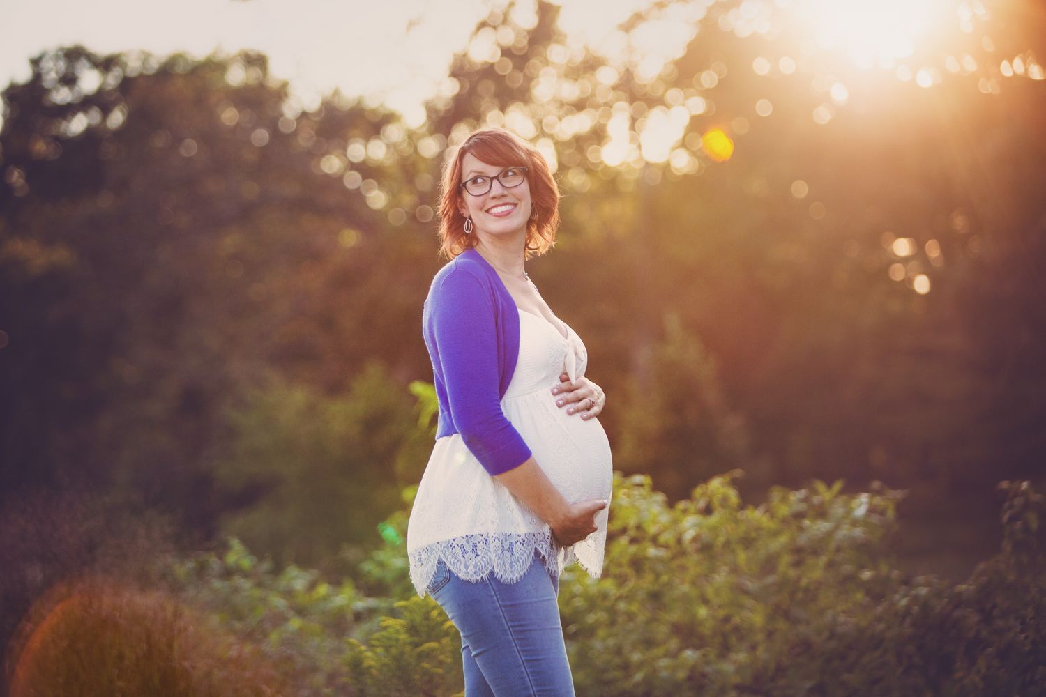 Silhouetted portrait of an expectant mother in casual wear against a golden sunset in nature.