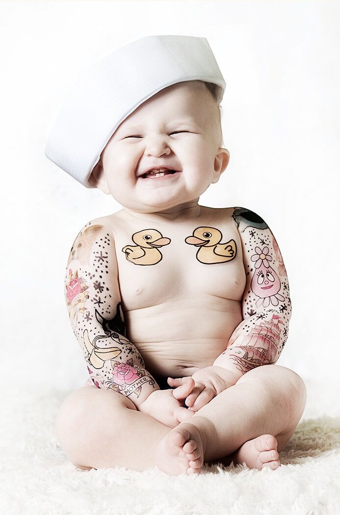 Baby wearing white hat smiles while sitting on fluffy white carpet with decorative stickers.