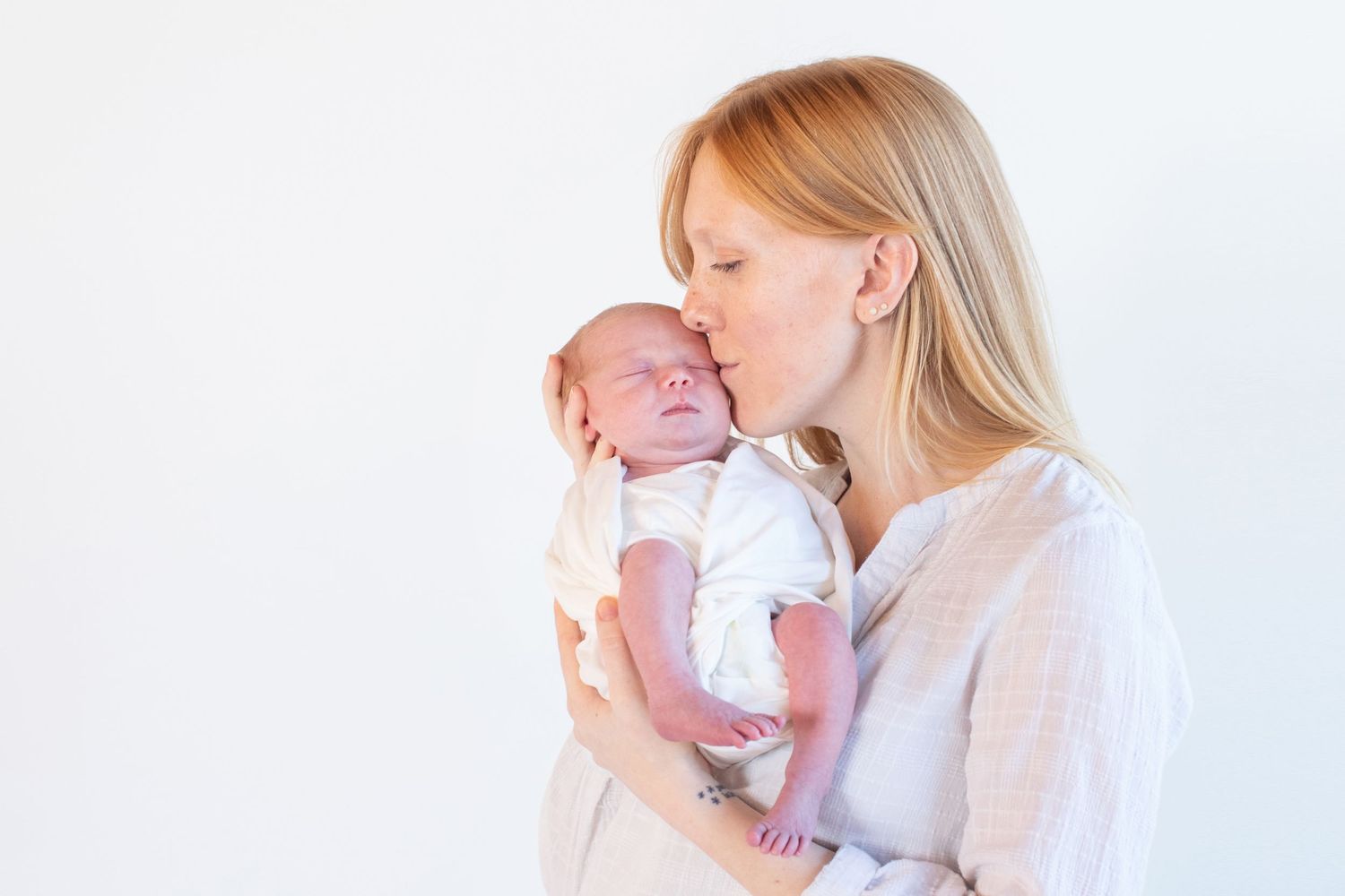 A tender moment between parent and newborn baby in soft white lighting.
