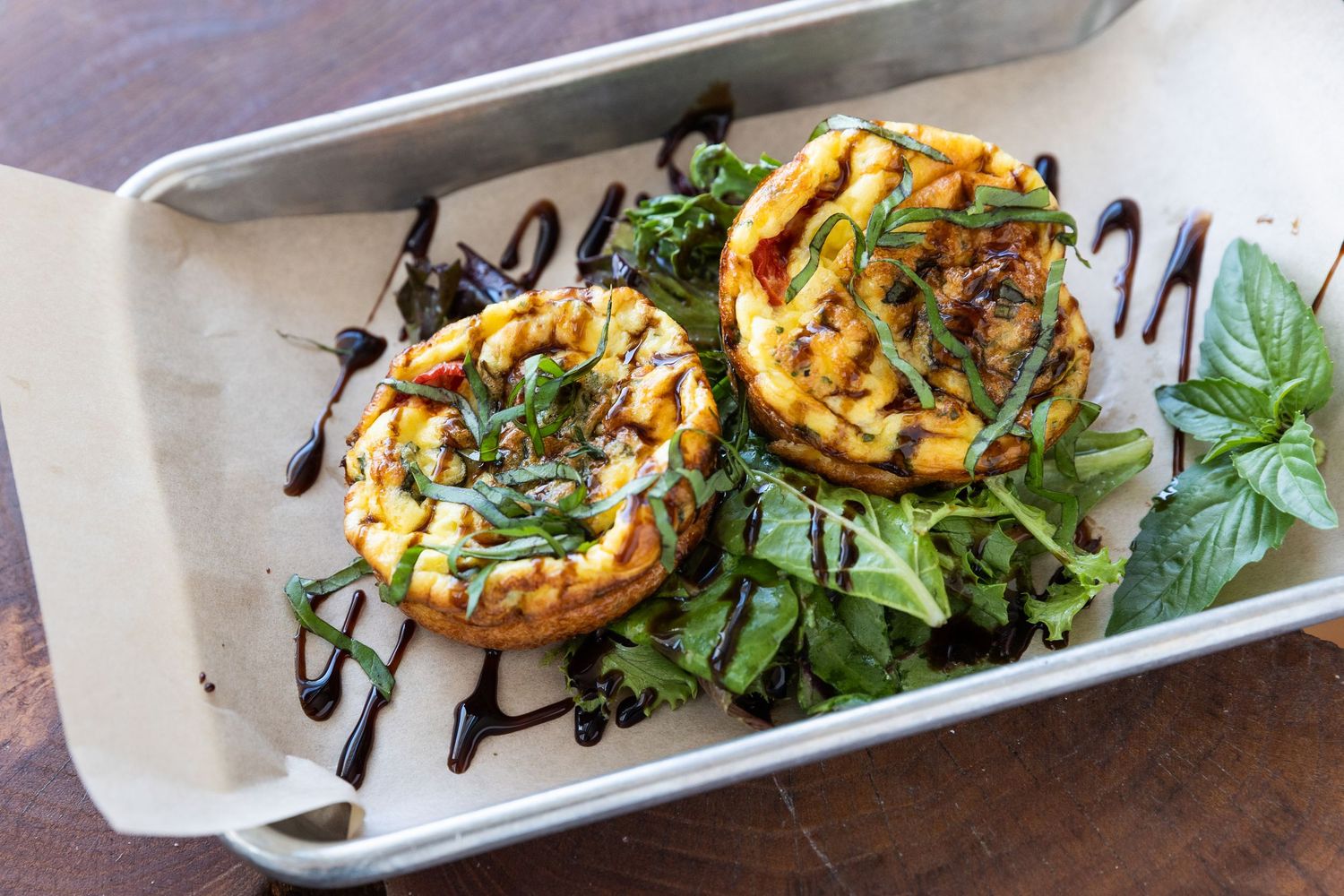 Grilled zucchini slices topped with herbs, balsamic glaze and fresh greens arranged on a white serving platter.