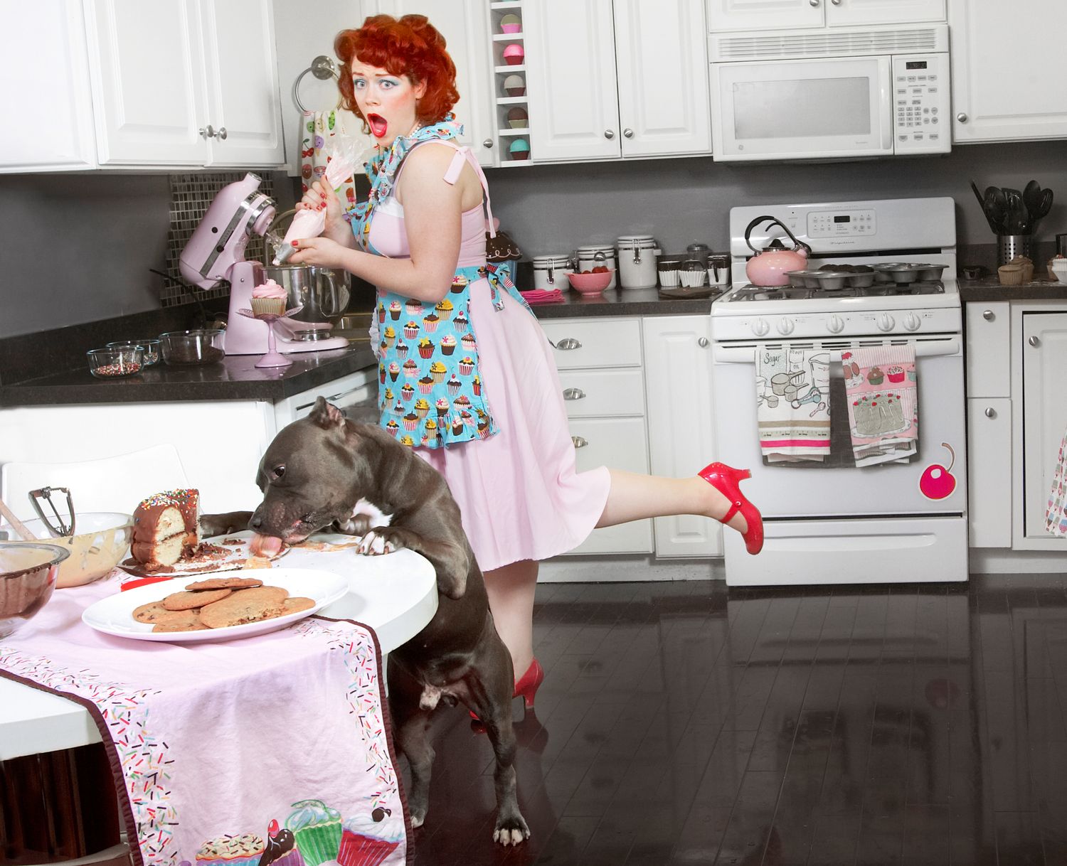 Vintage-styled kitchen scene with great dane and pink polka dot dress near dining table.