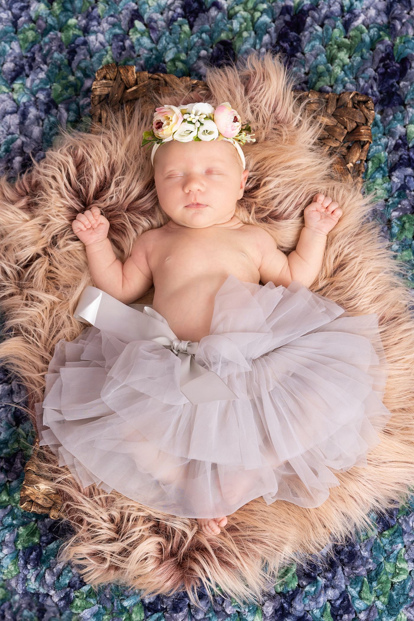 A baby in a white tulle dress lying on furry fabric with floral background decorations.