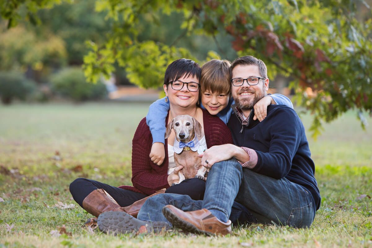 Family sitting outdoors with small dog in autumn setting.