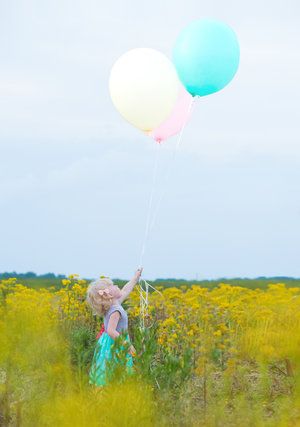 Colorful balloons float above a vibrant yellow wildflower field on a sunny day.