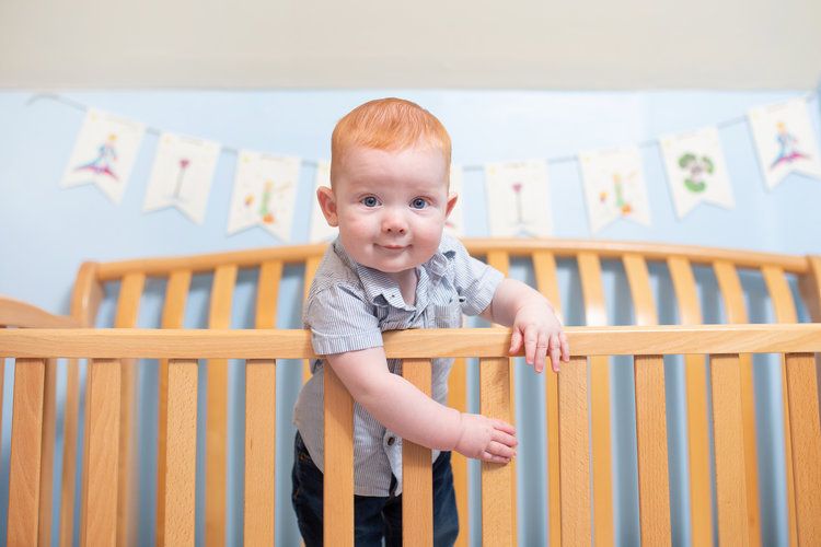 Toddler standing in wooden crib with banner decoration in background.