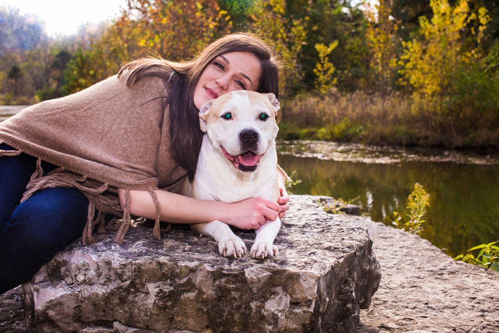 White dog and person posing together on rock by autumn pond.