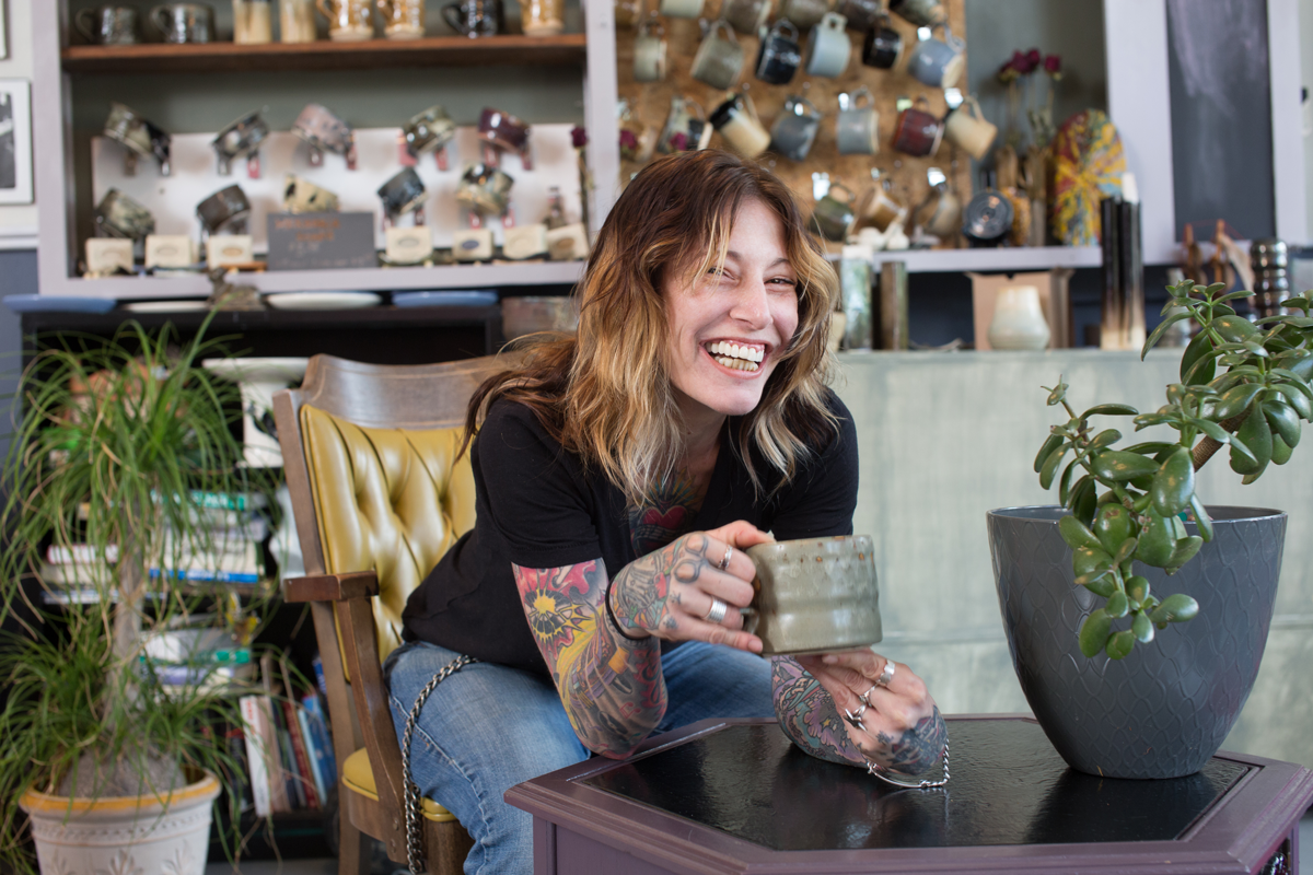 Person laughing while holding a drink in a room filled with decorative objects and plants.