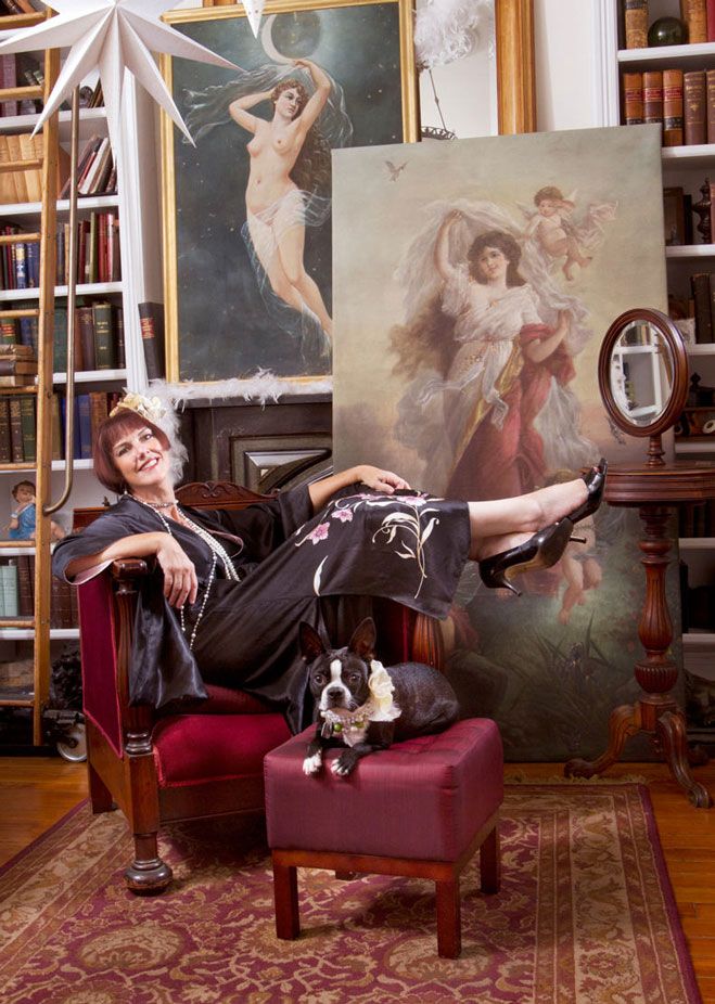 A Boston Terrier sits with someone in a vintage-styled room filled with classical artwork and furniture.