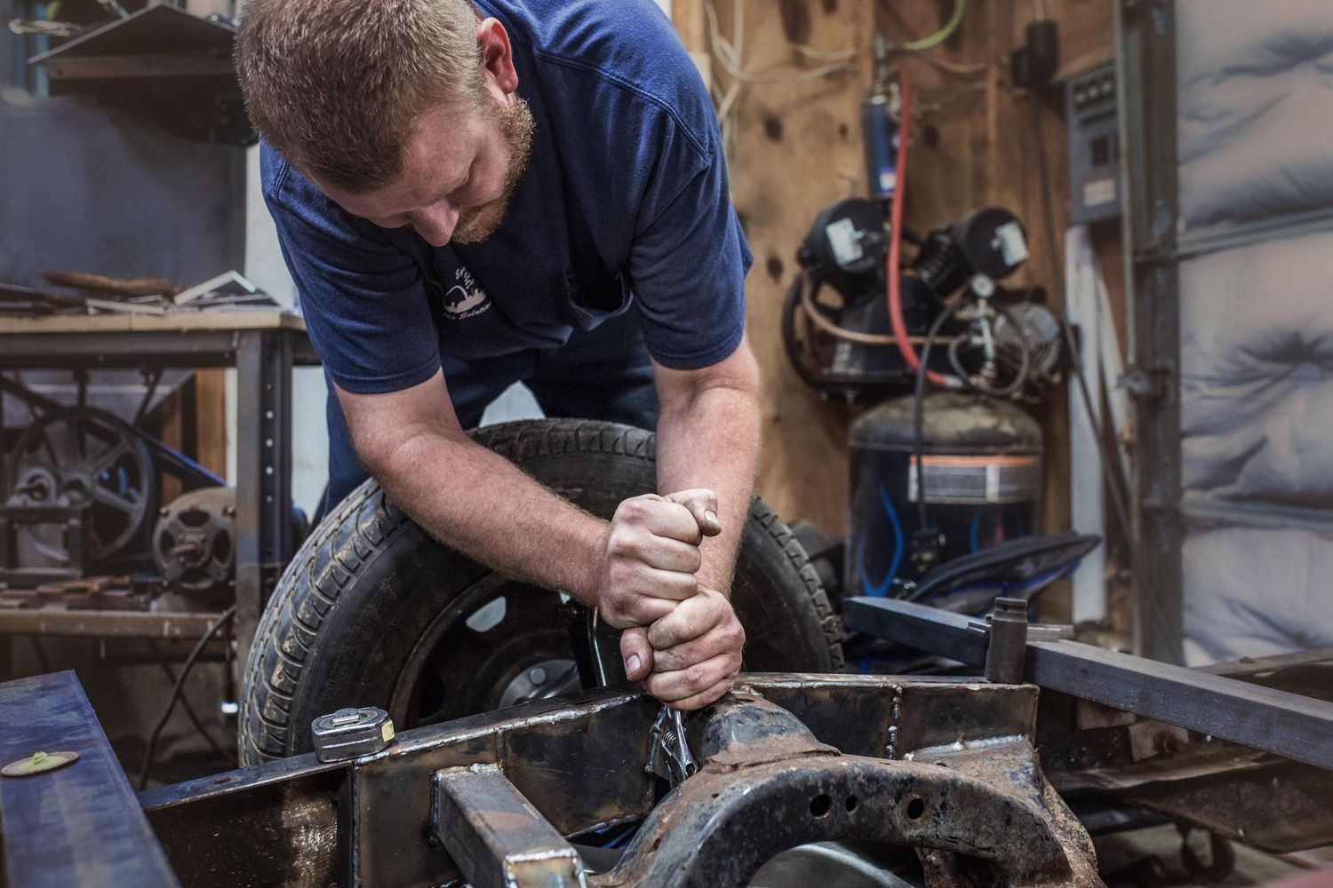 Worker in blue uniform uses tools on machinery in industrial workshop setting.