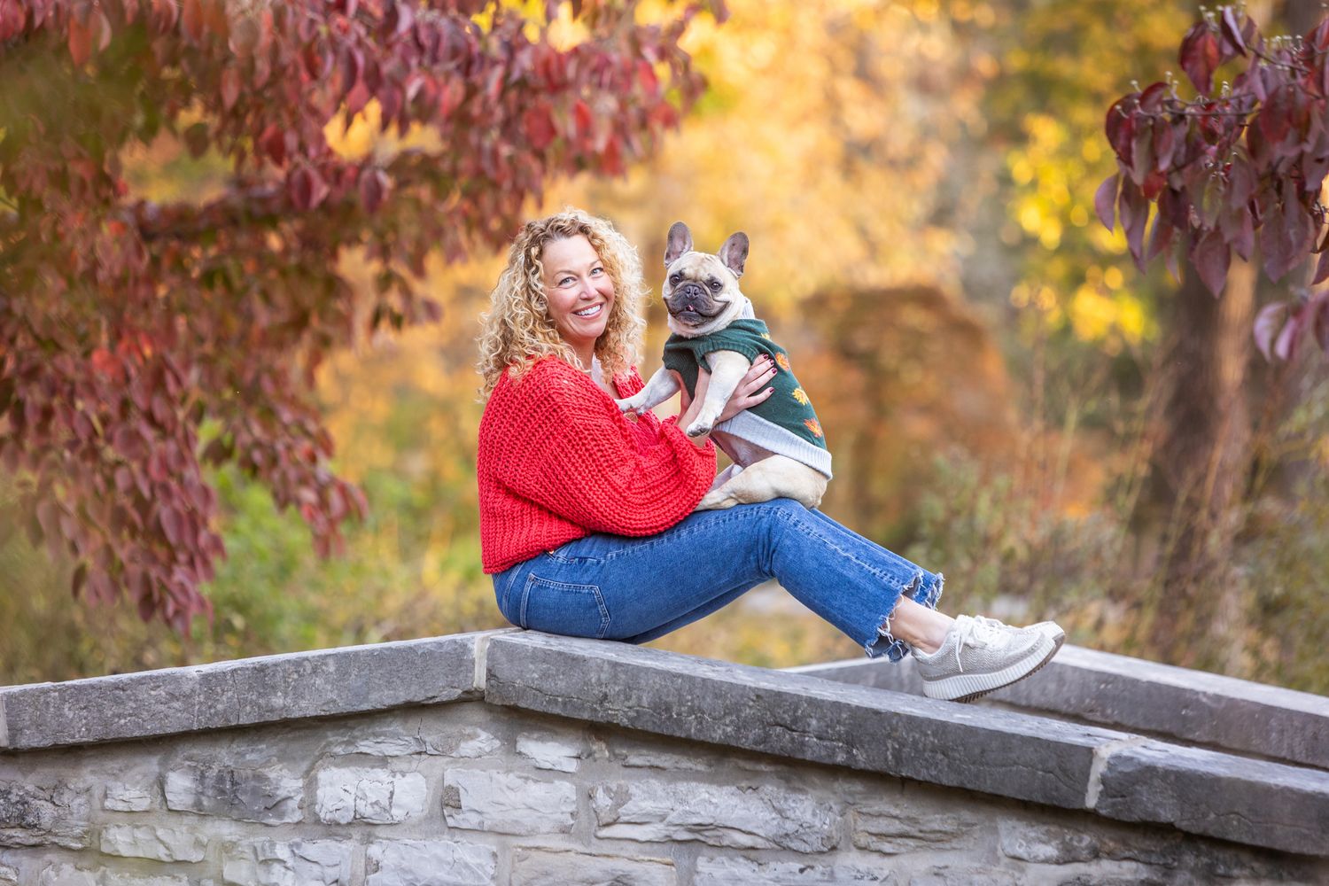 Someone sits with their lovable husky mix dog on a stone wall during autumn.
